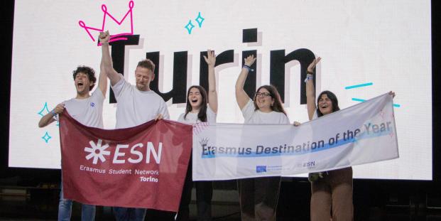 People cheering on a scenario in front of a big screen that says "Turin"